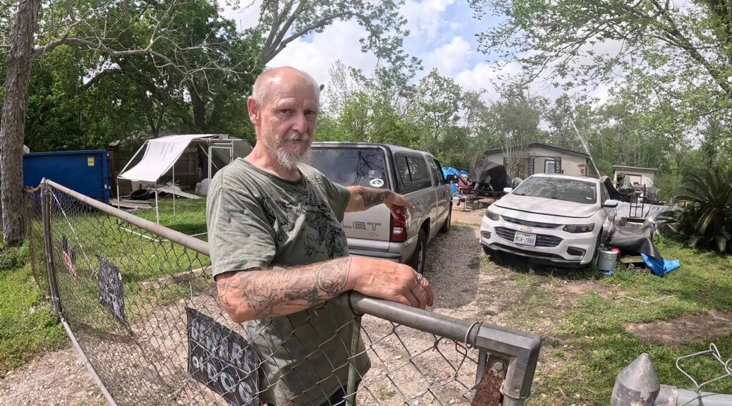 Raymond Elmore, cousin of James Elmore Jr., stands behind a chain-link fence looking into the camera.
