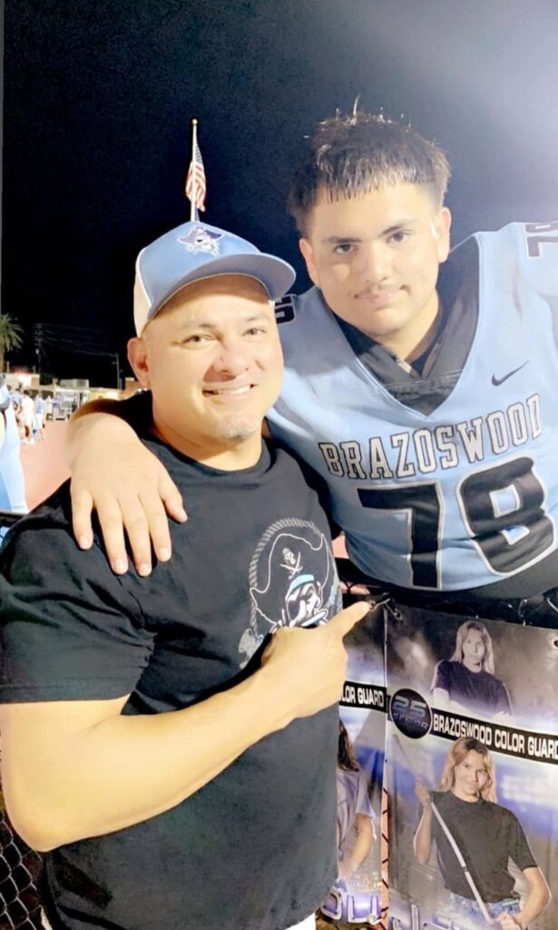 John Gabriel Mendoza Jr. poses with an adult male while wearing a Brazoswood High School football uniform.