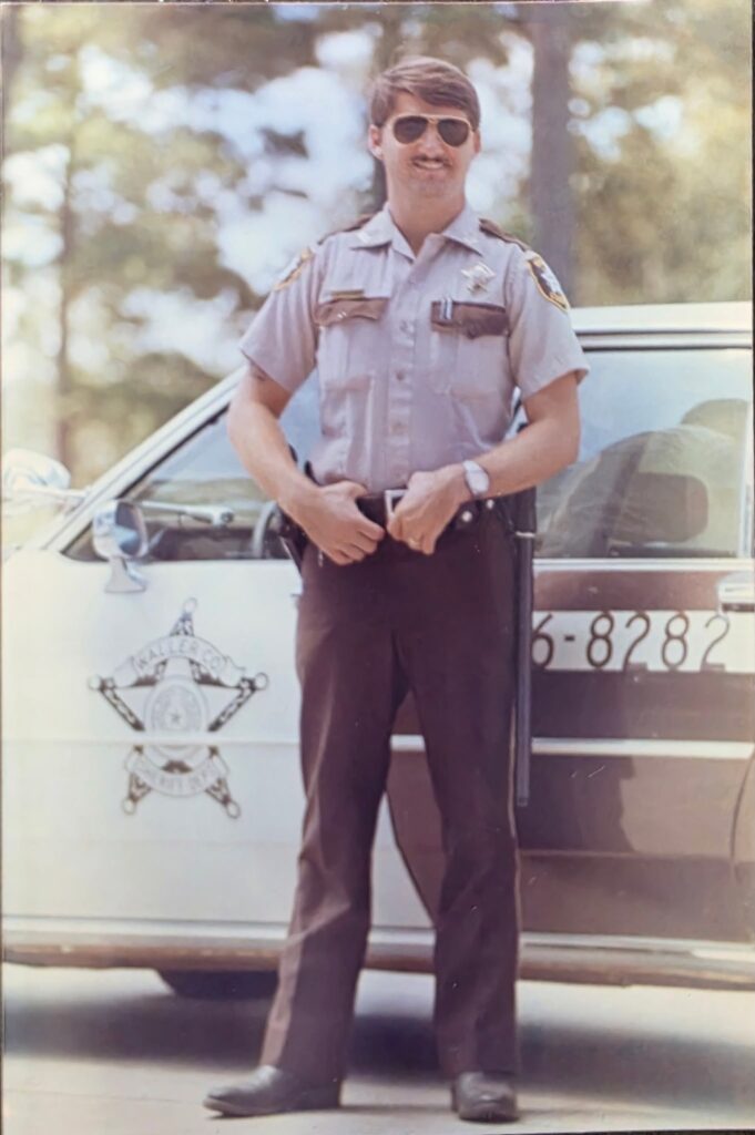 Vintage photograph of Kent McGowen in a Waller County Sheriff’s Office uniform standing beside a marked patrol vehicle while serving with the department before joining the Houston Police Department.
