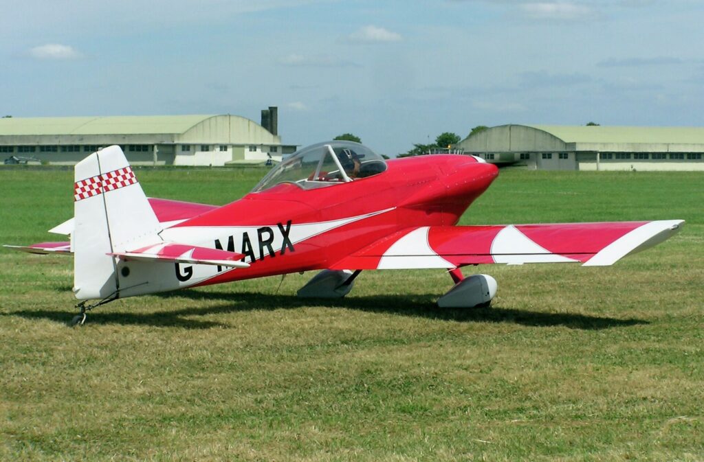 Red-and-white Van’s RV-4 experimental airplane parked on grass at an airfield.