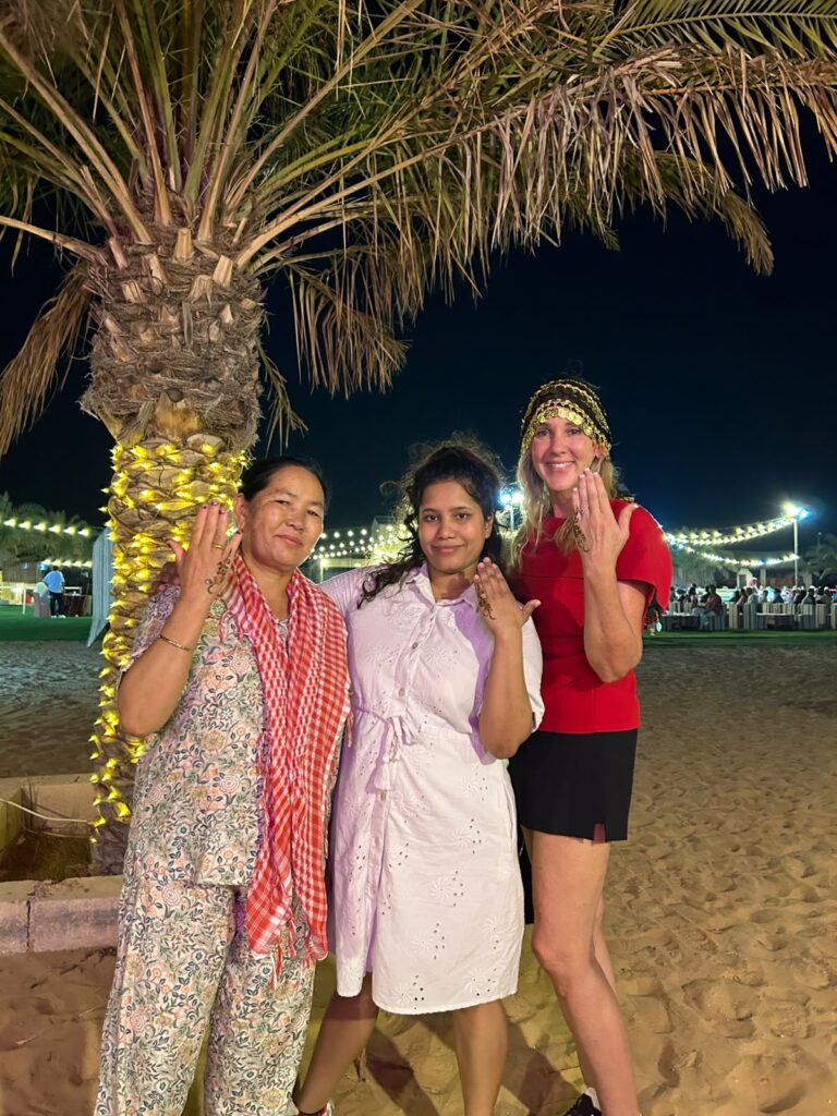 Investigative Reporter Tammy Rose posing with two women during a nighttime Dubai desert safari beneath palm trees.